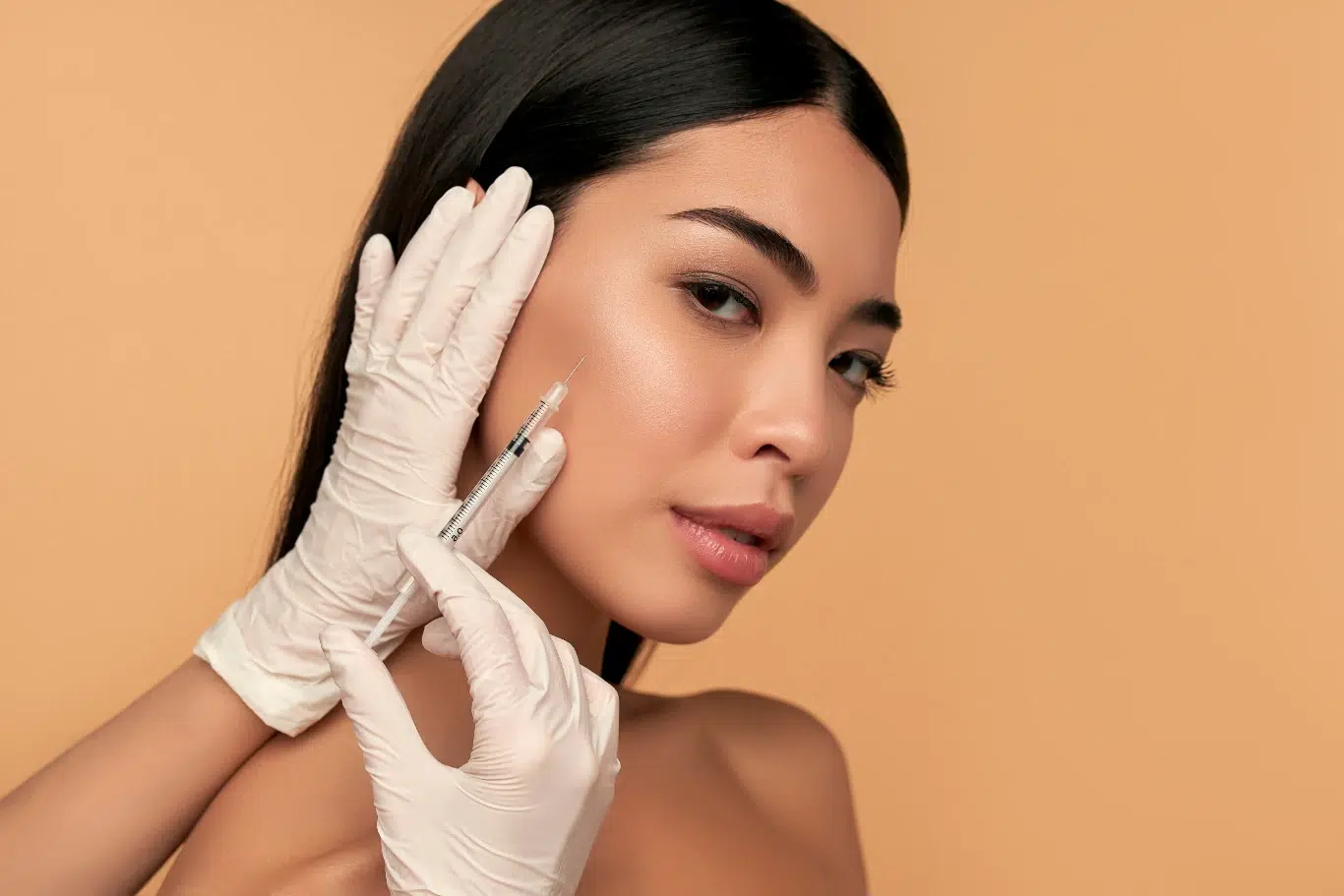 A close up photograph of a woman with dark hair receiving a facial injection